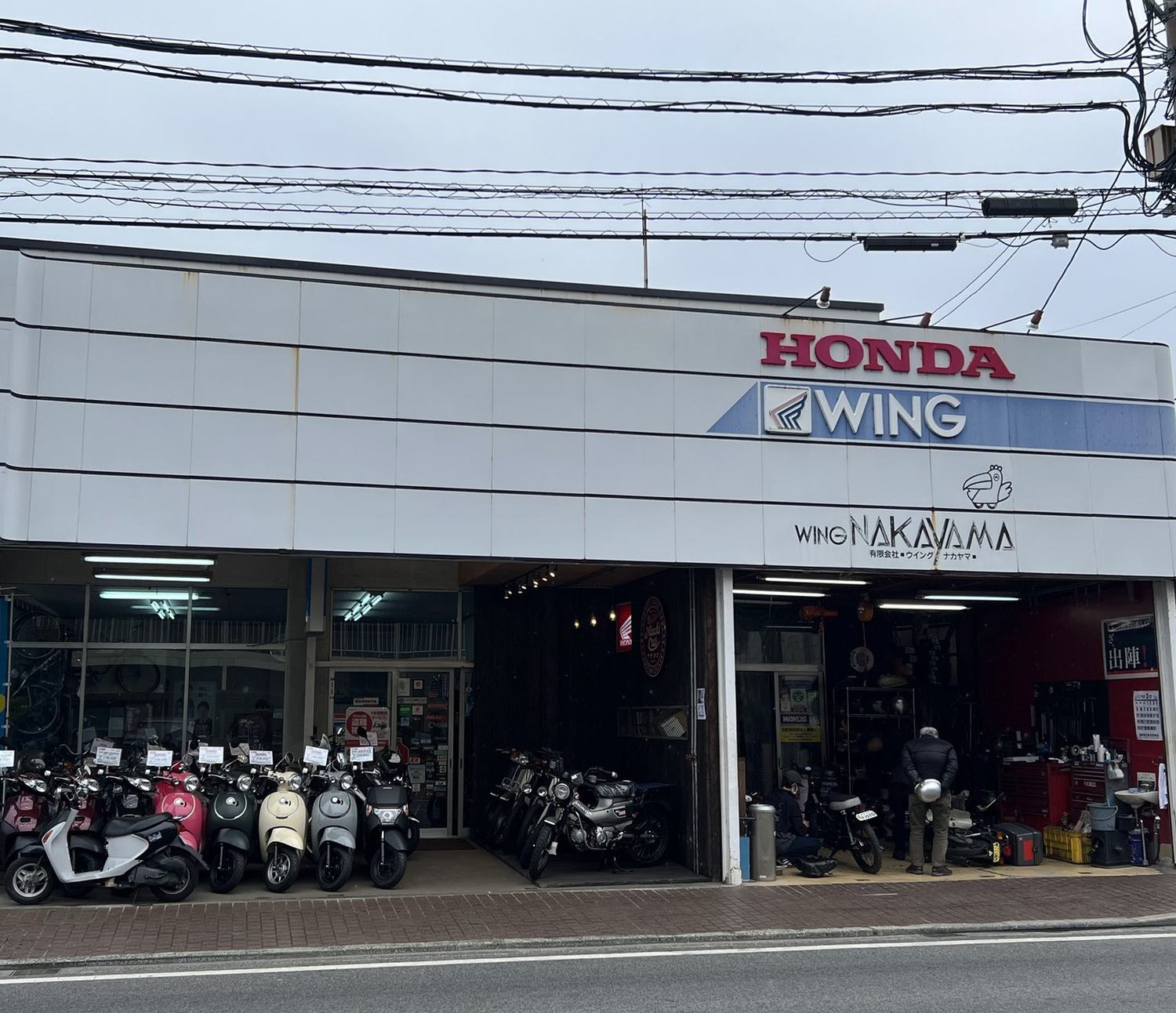 熊本市西区島崎のウイングナカヤマの店構え。HONDA WING の看板の下にスクーターが並び、右の作業場で整備をしている