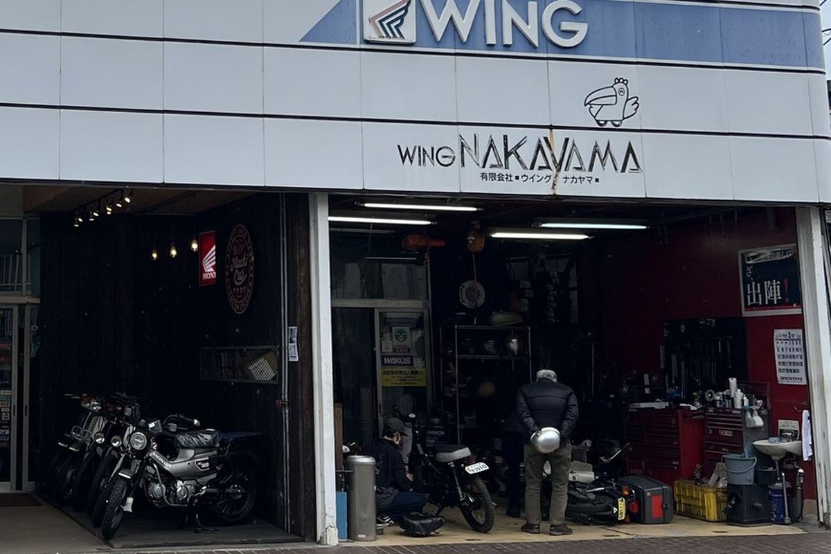 WING NAKAYAMA の看板の下の作業場で、バイクを整備しているところ